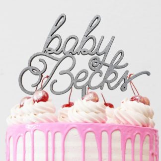 Taarttopper met baby en gepersonaliseerd met de achternaam van de baby op een roze drip cake